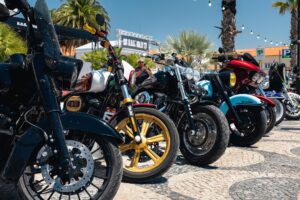 Diversas motocicletas Harley-Davidson customizadas e brilhantes exibidas sob o sol durante o European H.O.G. Rally em Cascais, Portugal, com público ao fundo.
