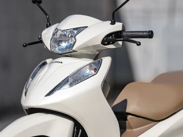 Honda Biz 2027 na cor vermelha estacionada em rua urbana, mostrando suas novas rodas de liga leve e design moderno, ideal para a mobilidade diária.