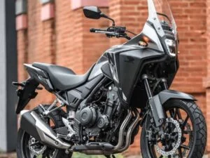 Uma motocicleta Honda NX500 2027 de cor vibrante, estacionada em uma estrada de terra com montanhas ao fundo, destacando seu design robusto e pneus de uso misto, pronta para aventura.
