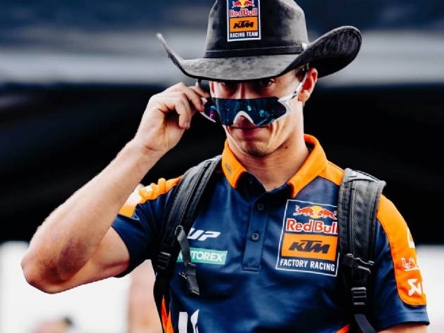 Pedro Acosta em sua moto de MotoGP, em alta velocidade, realizando uma curva durante uma corrida, com outros pilotos ao fundo e a torcida nas arquibancadas.