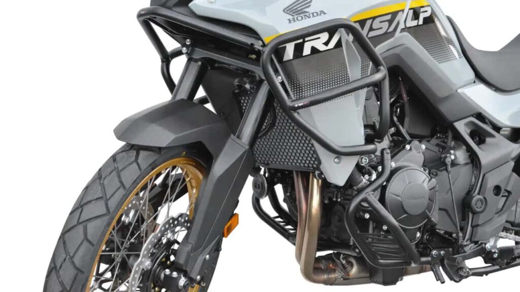 Honda Transalp XL750 branca equipada com acessórios de proteção Top Block, incluindo barras de proteção de motor e carenagem e um protetor de cárter, estacionada em um cenário ao ar livre.