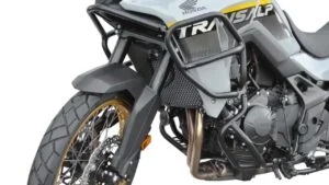 Honda Transalp XL750 branca equipada com acessórios de proteção Top Block, incluindo barras de proteção de motor e carenagem e um protetor de cárter, estacionada em um cenário ao ar livre.