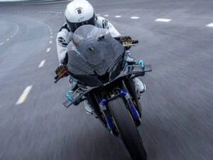 Detalhe de um protótipo de motocicleta superesportiva CFMOTO V4 SR-RR, com linhas aerodinâmicas agressivas, carenagem em fibra de carbono e detalhes em vermelho e cinza, transmitindo alta velocidade e tecnologia de ponta em um ambiente de pista de testes.