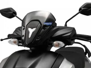 Imagem detalhada da scooter Yamaha ZR 125 2027, exibindo seu design moderno, farol de LED, carenagem aerodinâmica e os emblemas que indicam a tecnologia híbrida, em um cenário urbano dinâmico.