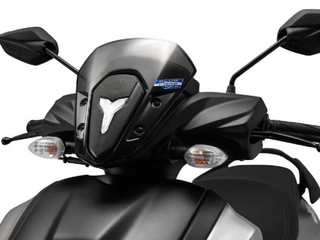 Imagem detalhada da scooter Yamaha ZR 125 2027, exibindo seu design moderno, farol de LED, carenagem aerodinâmica e os emblemas que indicam a tecnologia híbrida, em um cenário urbano dinâmico.