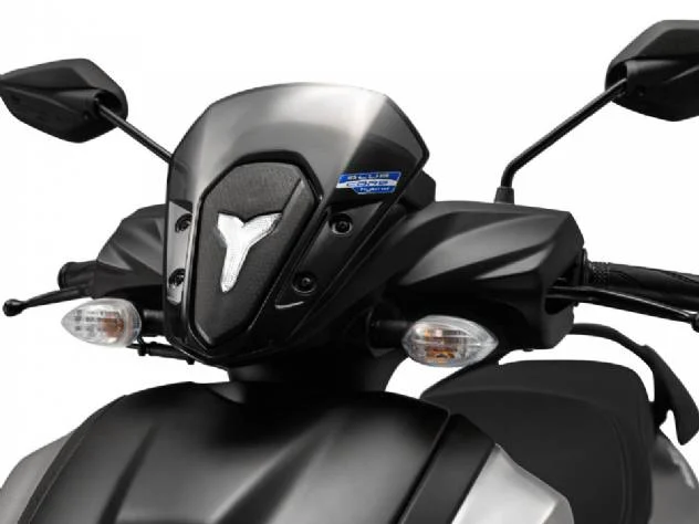 Imagem detalhada da scooter Yamaha ZR 125 2027, exibindo seu design moderno, farol de LED, carenagem aerodinâmica e os emblemas que indicam a tecnologia híbrida, em um cenário urbano dinâmico.