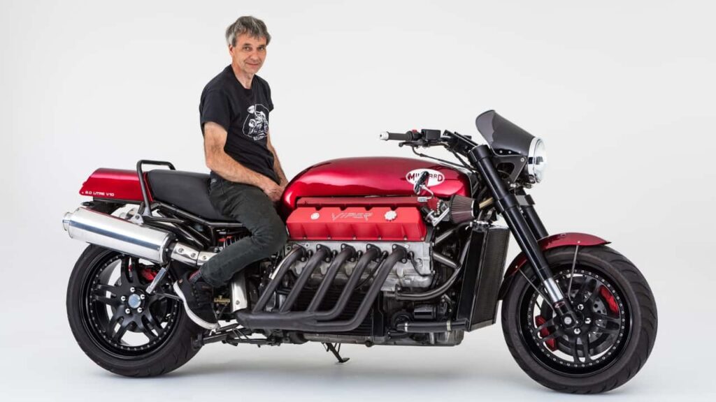 Imagem detalhada da motocicleta Millyard Viper V10, destacando seu enorme motor V10 do Dodge Viper e o chassi customizado, estacionada em um ambiente que realça sua grandiosidade e engenharia bespoke.