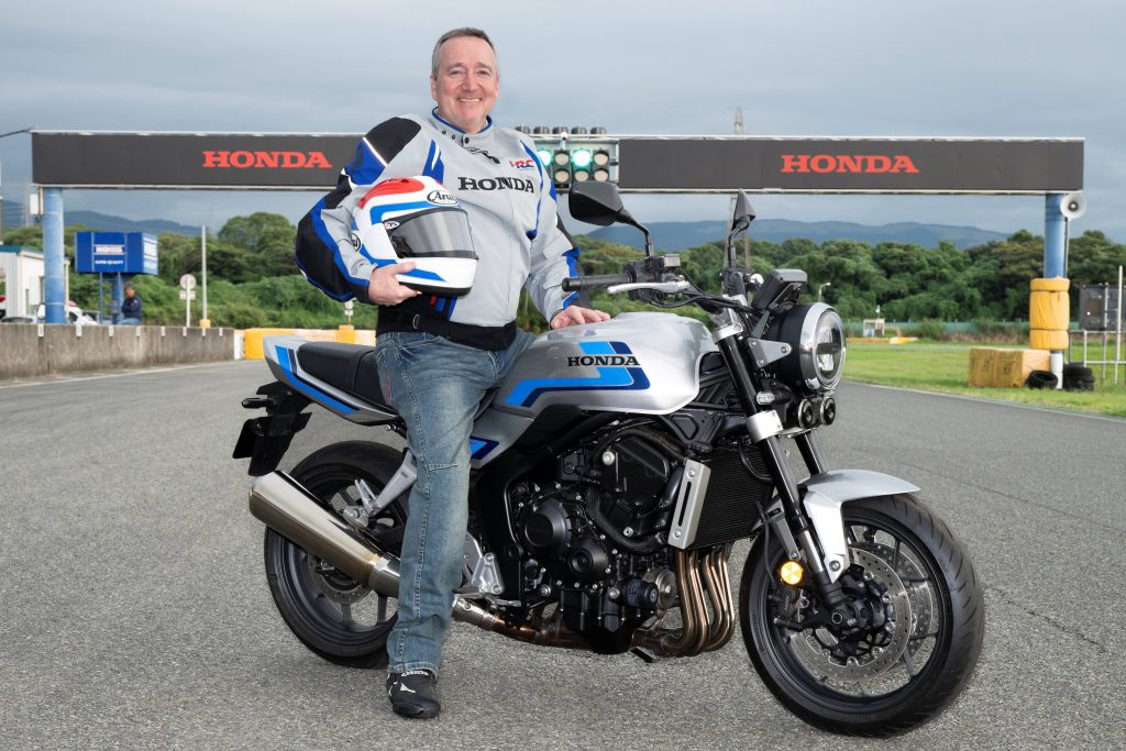 Uma imagem mostrando uma representação artística da presença da Honda no Goodwood Festival of Speed, com carros de F1, motos e protótipos elétricos no pit lane.