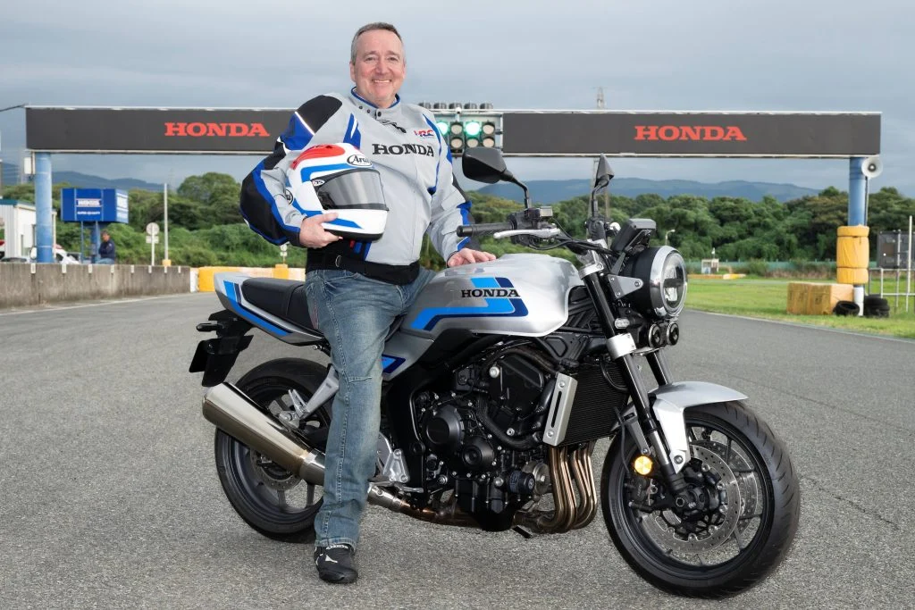 Uma imagem mostrando uma representação artística da presença da Honda no Goodwood Festival of Speed, com carros de F1, motos e protótipos elétricos no pit lane.