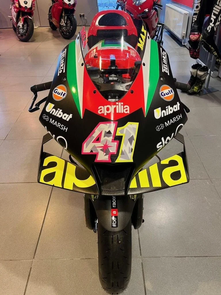 Aprilia RS-GP20 de corrida, uma motocicleta de MotoGP em plena pista, pilotada por Aleix Espargaró, destacando seu design aerodinâmico e a pintura de fábrica.