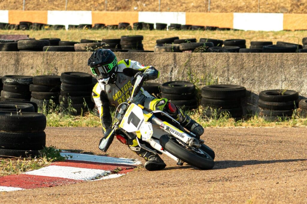 Motociclista em ação durante uma corrida do Campeonato Nacional Supermoto, realizando uma derrapagem controlada em uma curva de asfalto iluminada pela noite no Kartódromo de Vila Nova de Poiares.