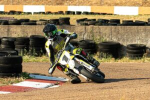 Motociclista em ação durante uma corrida do Campeonato Nacional Supermoto, realizando uma derrapagem controlada em uma curva de asfalto iluminada pela noite no Kartódromo de Vila Nova de Poiares.