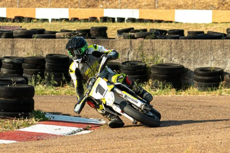 Motociclista em ação durante uma corrida do Campeonato Nacional Supermoto, realizando uma derrapagem controlada em uma curva de asfalto iluminada pela noite no Kartódromo de Vila Nova de Poiares.