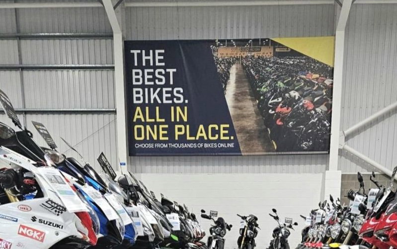 Fachada de uma grande concessionária de motos SuperBike Factory com diversos modelos expostos, retratando seu auge.