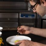 Imagem ilustrativa de um engenheiro trabalhando em um projeto de motocicleta Ducati Scrambler e, em contraste, um chef renomado preparando um prato gourmet em uma cozinha de luxo, simbolizando a transição de Guido Paternollo.