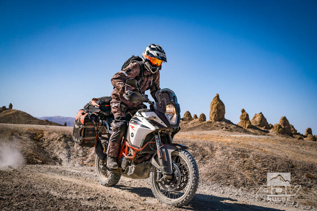 Motocicleta bigtrail estacionada entre as imponentes formações rochosas de tufa dos Trona Pinnacles, sob um céu azul e ensolarado no deserto de Mojave.