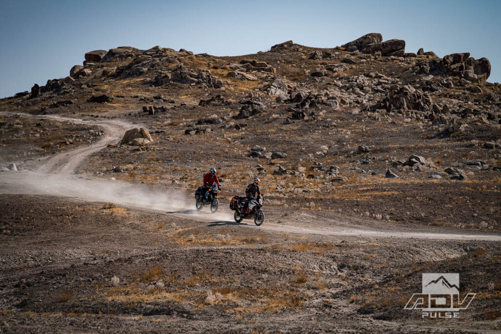 Motocicleta bigtrail estacionada entre as imponentes formações rochosas de tufa dos Trona Pinnacles, sob um céu azul e ensolarado no deserto de Mojave.