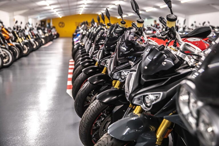 Vista panorâmica de uma grande concessionária de motocicletas usadas, SuperBike Factory, com centenas de motos de diversas marcas e modelos expostas no showroom. Detalhe da organização e iluminação do espaço.