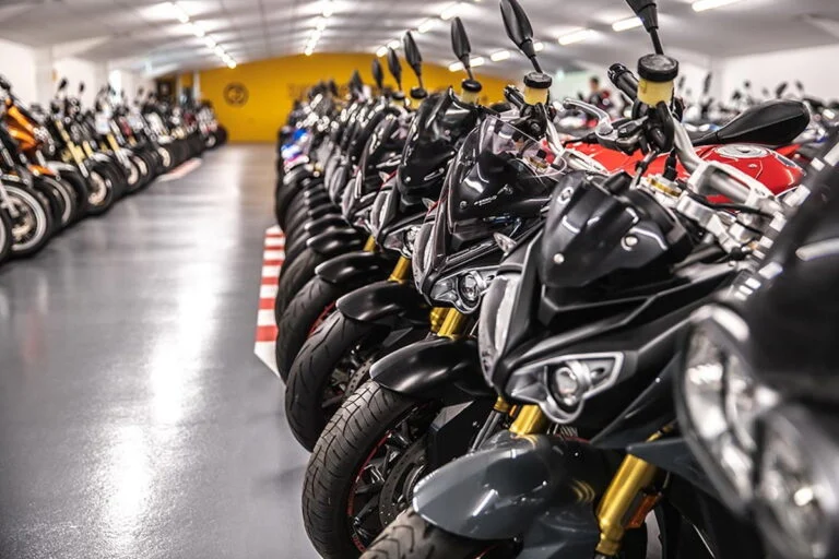 Vista panorâmica de uma grande concessionária de motocicletas usadas, SuperBike Factory, com centenas de motos de diversas marcas e modelos expostas no showroom. Detalhe da organização e iluminação do espaço.