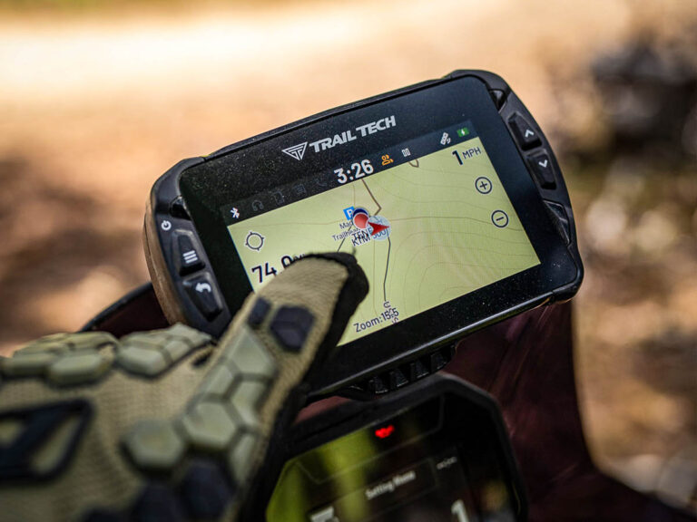 Close-up do sistema GPS off-road Trail Tech Voyager Pro4 montado em uma motocicleta, exibindo sua tela colorida e robustez.