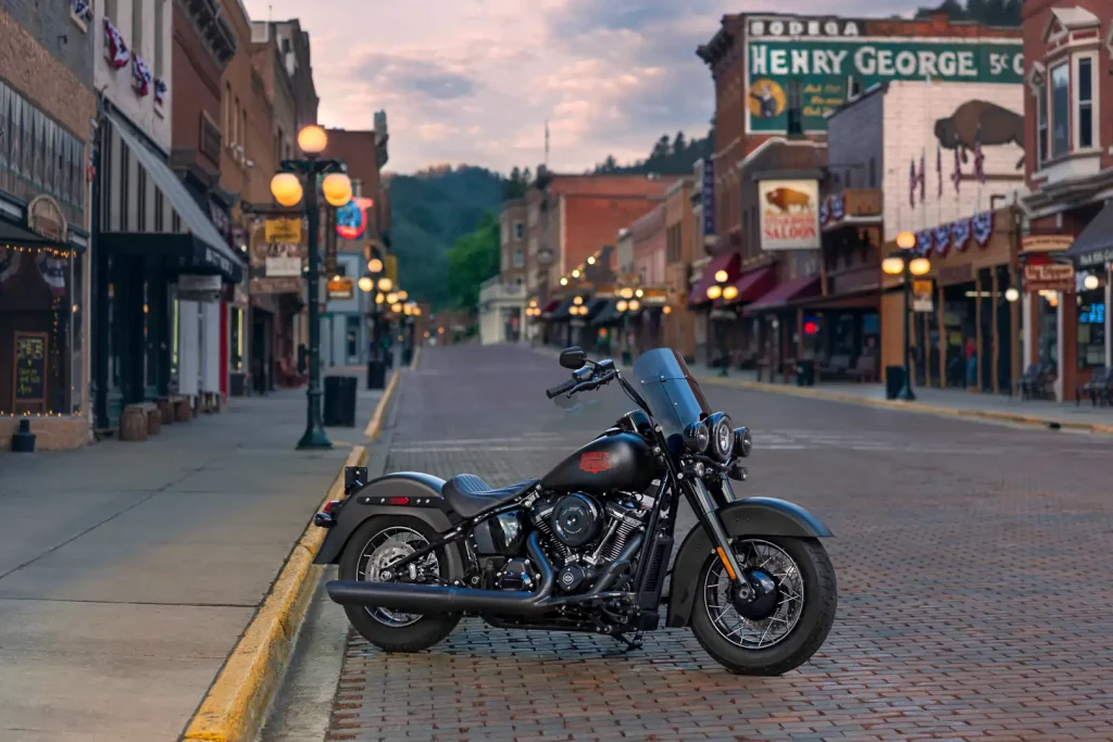 Harley-Davidson Deadwood 2026 estacionada, destacando seu acabamento Denim Black e o design clássico da linha Softail, ideal para pilotos que buscam tradição.
