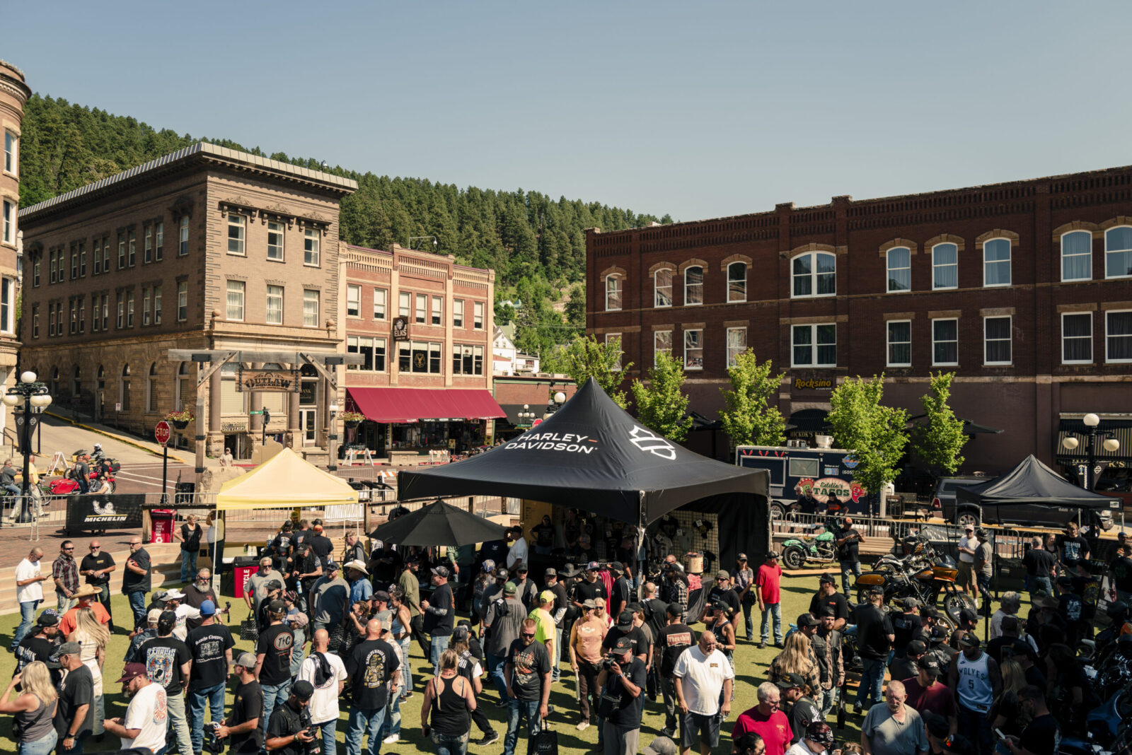 Multidão de motociclistas em suas Harley-Davidson reunidos durante a Sturgis Motorcycle Rally, com a paisagem das Black Hills ao fundo.