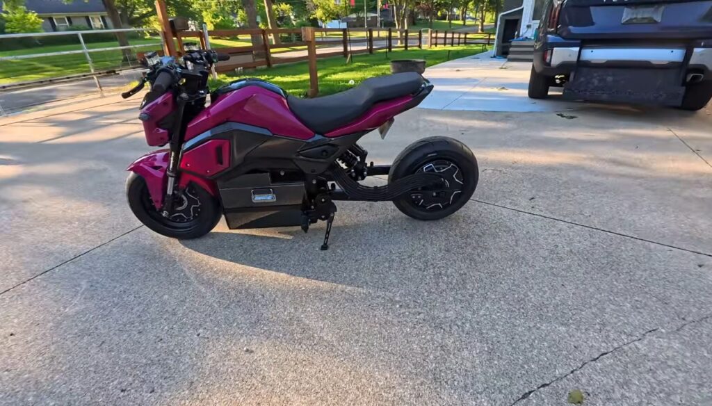 Uma Honda Grom elétrica customizada, com detalhes em azul e um motor elétrico visível no cubo da roda traseira, exibindo seu design compacto e esportivo.