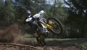 Piloto de enduro em ação com uma moto Husqvarna Enduro 2027 vermelha e branca, enfrentando um trilho técnico rochoso em alta velocidade, demonstrando a precisão do novo modelo.