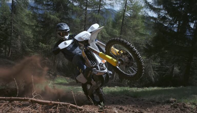 Piloto de enduro em ação com uma moto Husqvarna Enduro 2027 vermelha e branca, enfrentando um trilho técnico rochoso em alta velocidade, demonstrando a precisão do novo modelo.