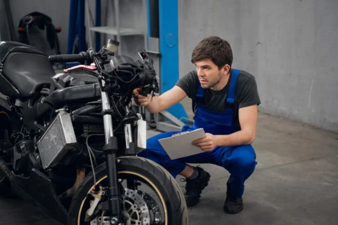 Motociclista europeu apresentando sua moto para inspeção técnica periódica, com inspetor verificando componentes de segurança.