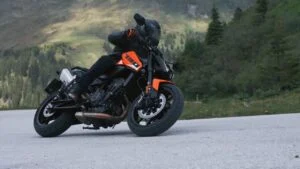 KTM 790 Duke 2027 em alta velocidade em uma curva, exibindo seu design naked e agilidade. O piloto está inclinado, demonstrando o controle preciso da motocicleta.