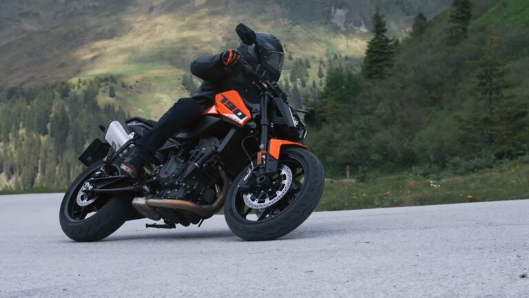 KTM 790 Duke 2027 em alta velocidade em uma curva, exibindo seu design naked e agilidade. O piloto está inclinado, demonstrando o controle preciso da motocicleta.