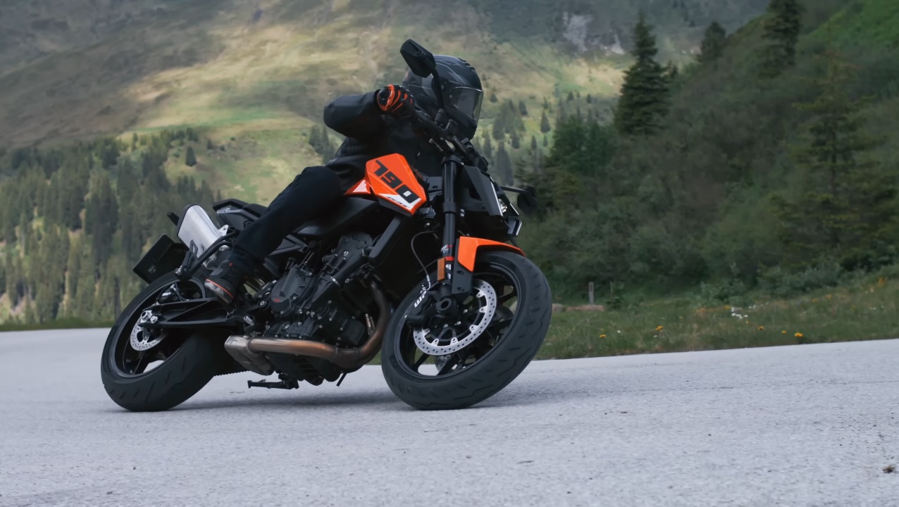 KTM 790 Duke 2027 em alta velocidade em uma curva, exibindo seu design naked e agilidade. O piloto está inclinado, demonstrando o controle preciso da motocicleta.