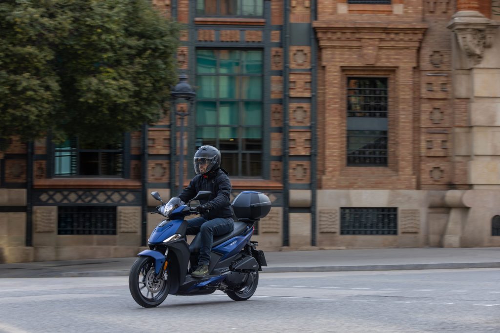 Kymco Agility 125 NX 2024 estacionada em ambiente urbano, exibindo seu design moderno e iluminação LED, destacando as rodas de liga leve e a ergonomia otimizada para o dia a dia.