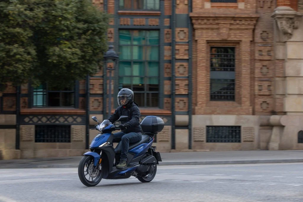 Kymco Agility 125 NX 2024 estacionada em ambiente urbano, exibindo seu design moderno e iluminação LED, destacando as rodas de liga leve e a ergonomia otimizada para o dia a dia.