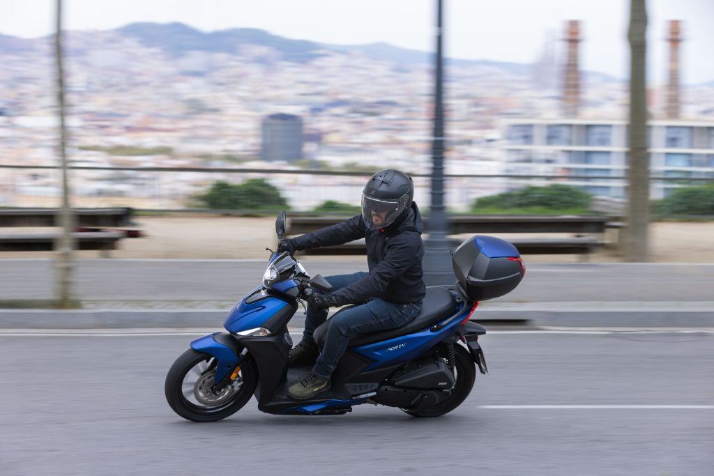 Kymco Agility 125 NX 2024 estacionada em ambiente urbano, exibindo seu design moderno e iluminação LED, destacando as rodas de liga leve e a ergonomia otimizada para o dia a dia.