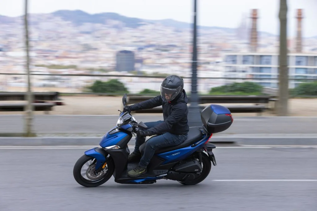 Kymco Agility 125 NX 2024 estacionada em ambiente urbano, exibindo seu design moderno e iluminação LED, destacando as rodas de liga leve e a ergonomia otimizada para o dia a dia.