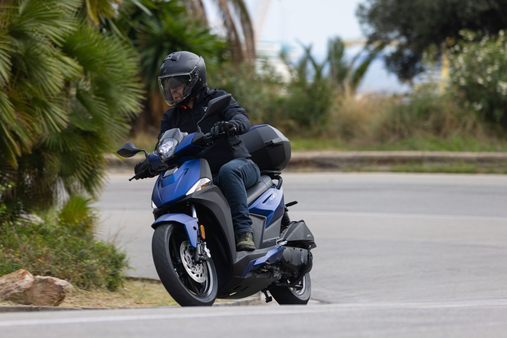 Kymco Agility 125 NX 2024 estacionada em ambiente urbano, exibindo seu design moderno e iluminação LED, destacando as rodas de liga leve e a ergonomia otimizada para o dia a dia.