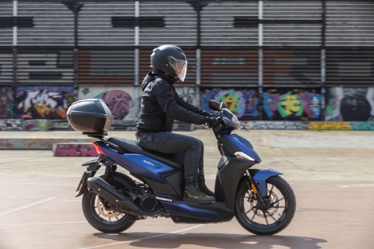 Kymco Agility 125 NX 2024 estacionada em ambiente urbano, exibindo seu design moderno e iluminação LED, destacando as rodas de liga leve e a ergonomia otimizada para o dia a dia.