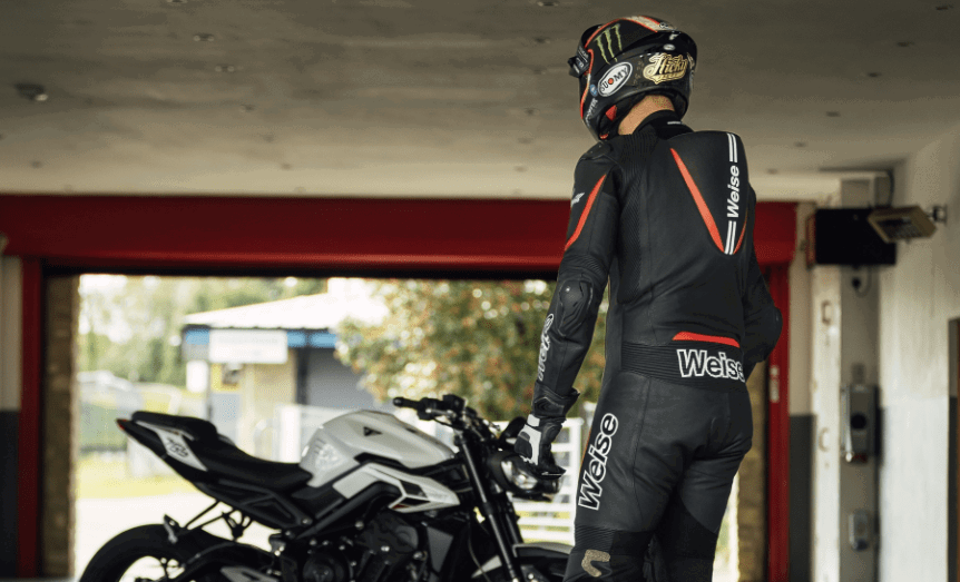 Macacão Weise Tornado 2.0 de couro preto e cinza, com detalhes em vermelho, em manequim, destacando sua construção de peça única e proteções, ideal para pilotagem esportiva.