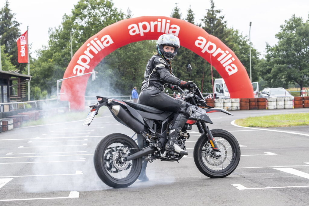 Piloto em uma supermoto de alta performance, executando uma curva inclinada em uma pista de asfalto, mostrando a agilidade e o controle do veículo.