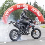 Piloto em uma supermoto de alta performance, executando uma curva inclinada em uma pista de asfalto, mostrando a agilidade e o controle do veículo.