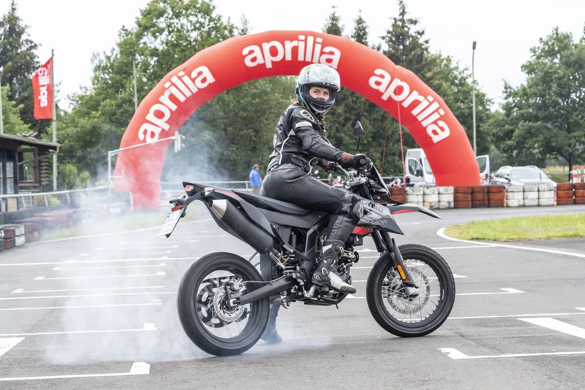 Piloto em uma supermoto de alta performance, executando uma curva inclinada em uma pista de asfalto, mostrando a agilidade e o controle do veículo.
