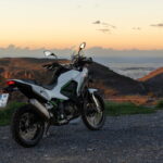 Motocicleta em uma estrada sinuosa nas montanhas dos Pireneus na Espanha, ao pôr do sol, destacando a beleza das melhores viagens de moto na Europa.