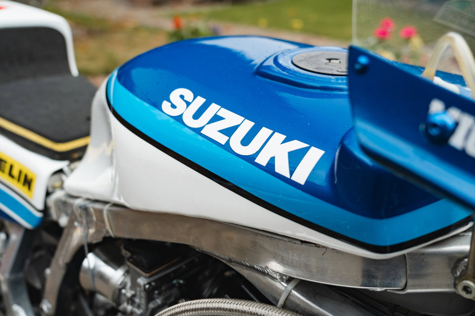 Mick Grant a bordo de sua icônica Heron Suzuki GS1000R de competição no lendário circuito do Isle of Man TT, uma moto de corrida histórica e de alto desempenho.