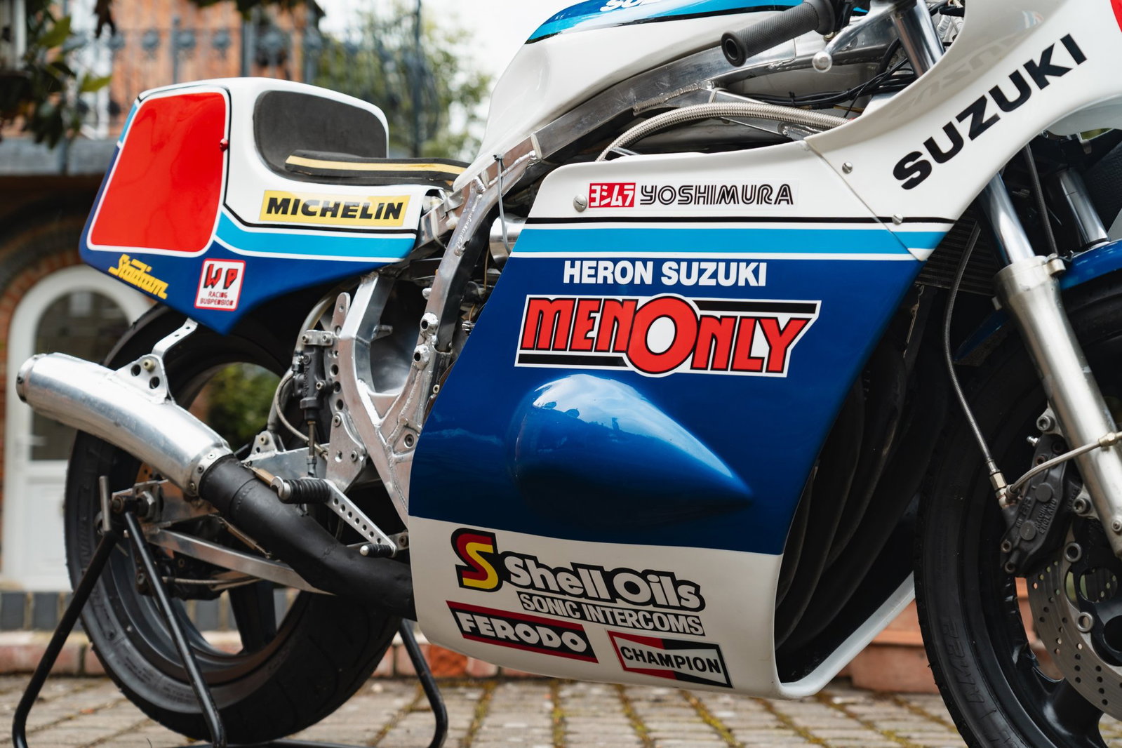 Mick Grant a bordo de sua icônica Heron Suzuki GS1000R de competição no lendário circuito do Isle of Man TT, uma moto de corrida histórica e de alto desempenho.