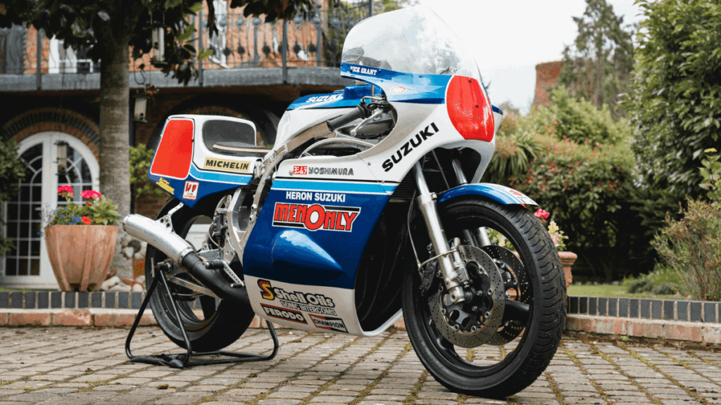 Mick Grant a bordo de sua icônica Heron Suzuki GS1000R de competição no lendário circuito do Isle of Man TT, uma moto de corrida histórica e de alto desempenho.