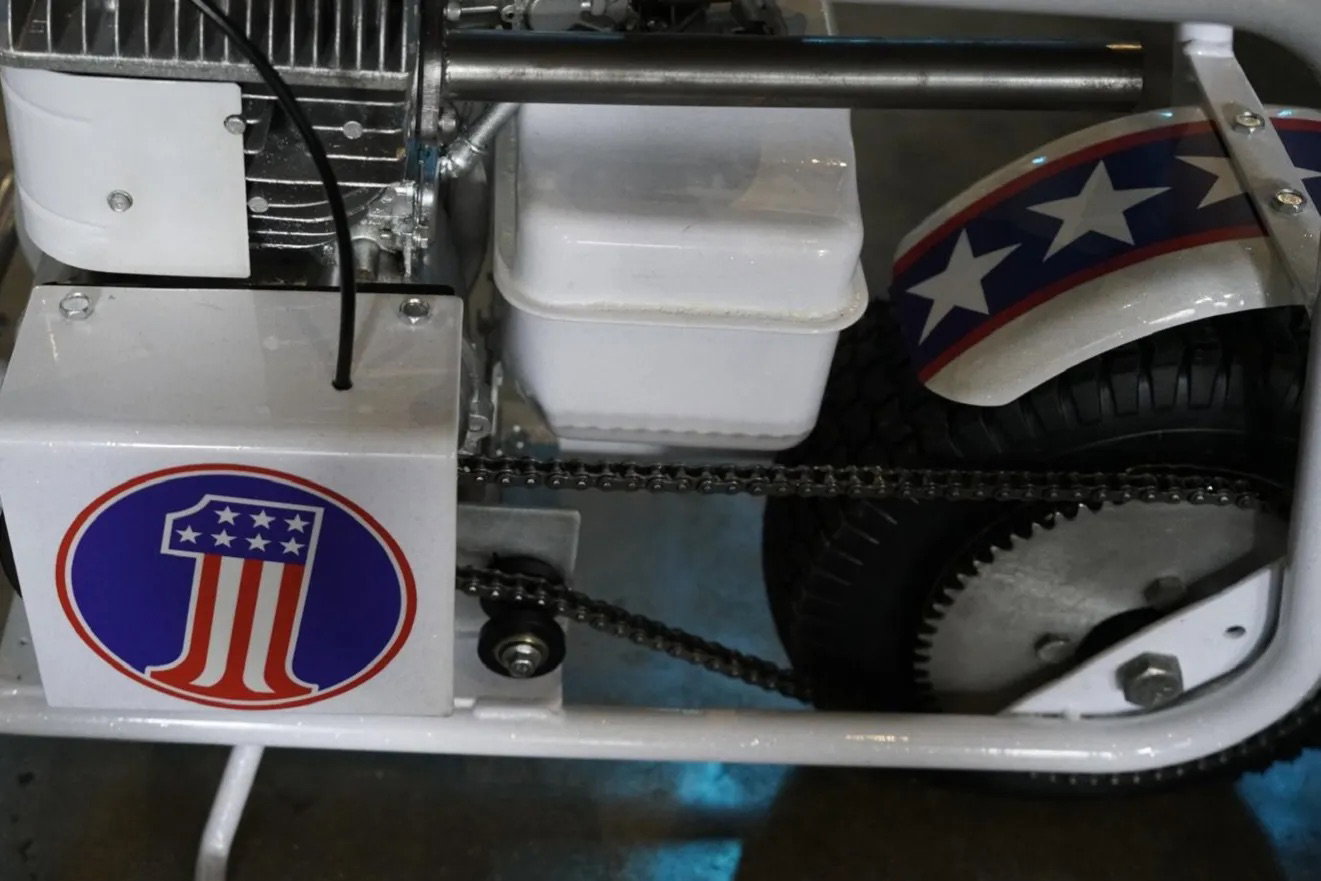 Minibike Ruttman 1972 restaurada, vermelha e branca, em exibição, com estilo remetendo aos anos 70 e ao legado de Evel Knievel.