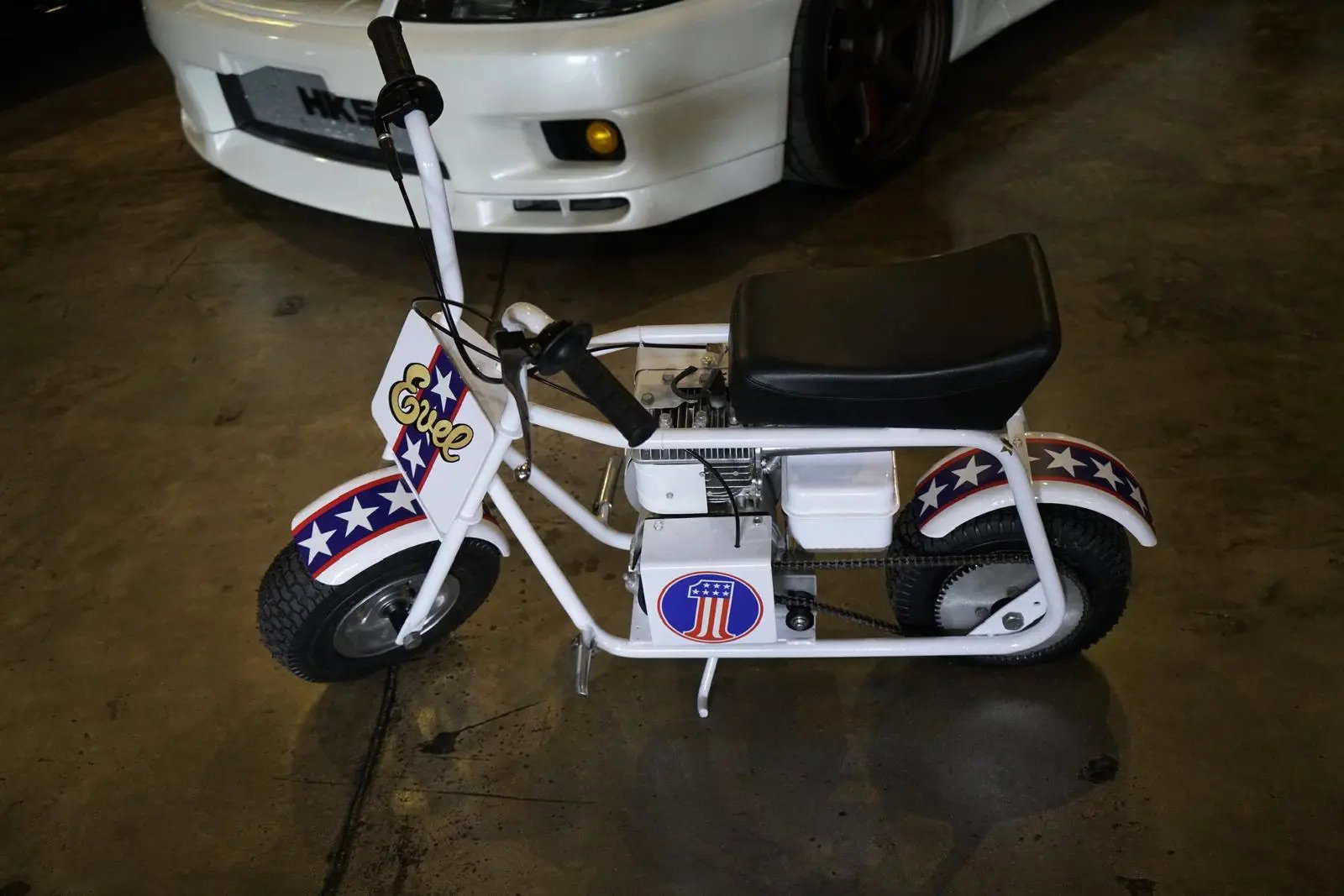 Minibike Ruttman 1972 restaurada, vermelha e branca, em exibição, com estilo remetendo aos anos 70 e ao legado de Evel Knievel.