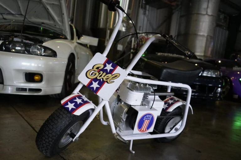 Minibike Ruttman 1972 restaurada, vermelha e branca, em exibição, com estilo remetendo aos anos 70 e ao legado de Evel Knievel.